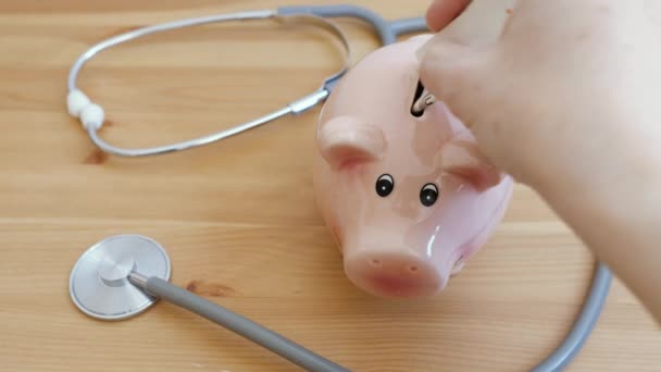 Medizinstethoskop Und Sparschwein Auf Dem Tisch Investition Krankenversicherung Und Vermögenskonzept — Stockvideo
