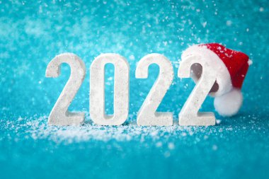 Beton numaralar 2022, kırmızı Noel Baba şapkalı mavi parlak arka plan ve düşen kar. Boşluğu kopyala