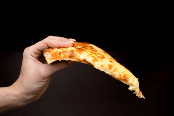 Un pedazo de pizza de queso en la mano sobre un fondo oscuro Imagen de archivo