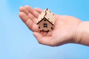 Mavi arka planda insan avuçlarında küçük ahşap bir ev.