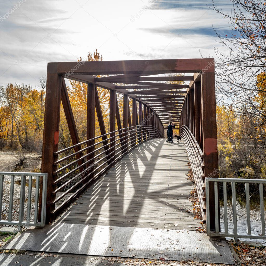 Dog walker on bridge over Boise River in fall