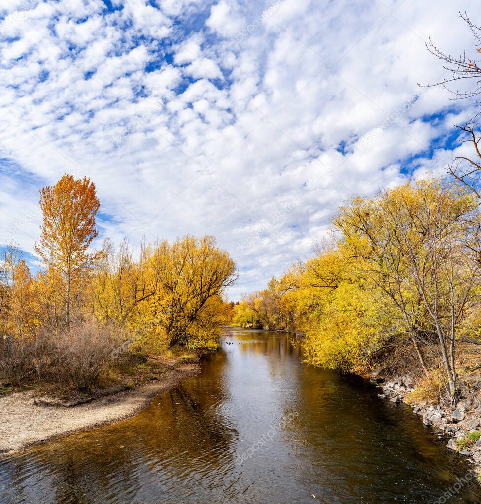 Blue sky and clouds above Boise River with autumn trees