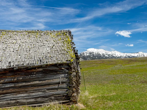 アイダホ州の田舎の素朴な丸太小屋の向こうの雪に覆われた山 — ストック写真