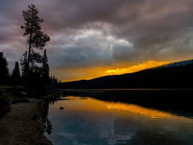 Idaho 'nun vahşi doğasında yüksek bir dağ gölünün üzerinde sabah güneşi doğuyor.