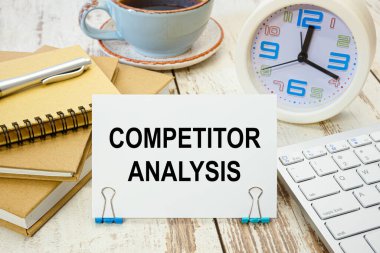 Ofis malzemelerinin olduğu masada üzerinde COMPETITOR ANALYSIS yazan bir tabela.