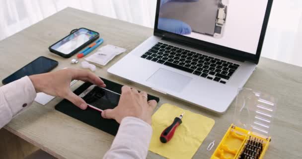 Τα χέρια Mens αποσυναρμολογούν ένα σπασμένο τηλέφωνο χρησιμοποιώντας ένα βίντεο προπόνησης σε ένα φορητό υπολογιστή — Αρχείο Βίντεο