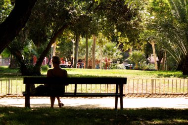 Young woman resting on a bench in a city garden on a sunny day