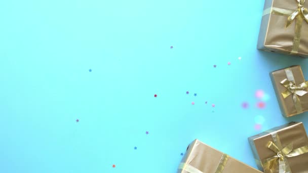 Святкові різнокольорові блискітки у вигляді зірок падають на синій фон із золотими подарунками — стокове відео
