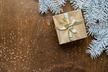 Tahta bir masanın üzerinde altın bir hediye kutusu. Yıldızlar şeklinde altın işlemeli. Köknar dalları arasında.