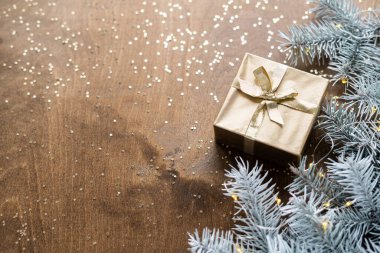 Tahta bir masanın üzerinde, köknar dallarının arasında sıcak ampulleri olan altın bir hediye kutusu.