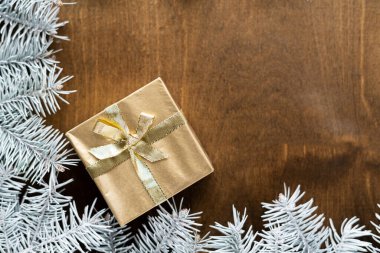 Tahta bir masanın üzerinde, köknar dallarının arasında sıcak ampulleri olan altın bir hediye kutusu. Yüksek kalite fotoğraf