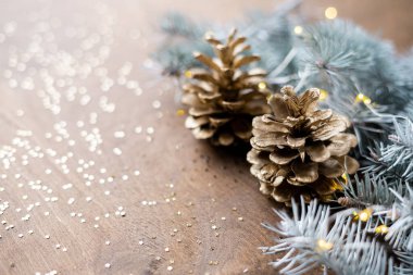 Tahta bir masanın üzerindeki altın sarısı kozalaklar. Yıldızlar şeklinde, köknar dalları arasında sıcak ampuller.