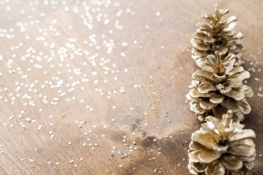 Tahta bir masanın üzerinde, yıldızlara benzeyen altın işlemeli doğal altın koniler, köknar dalları arasında. 