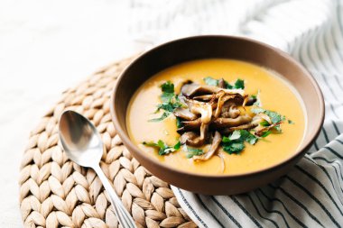 a plate of hot homemade pumpkin-coconut cream soup with fried mushrooms and fresh herbs. High quality photo