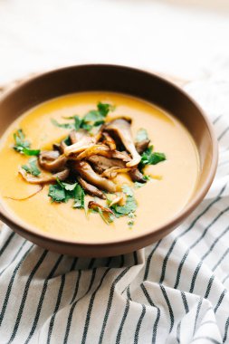 a plate of hot homemade pumpkin-coconut cream soup with fried mushrooms and fresh herbs