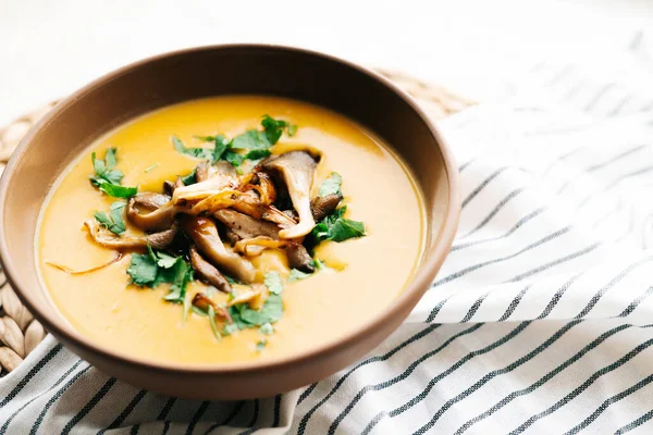 a plate of hot homemade pumpkin-coconut cream soup with fried mushrooms and fresh herbs. High quality photo