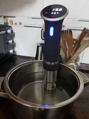 Düşük ısıda pişirmek için soous vide makinesi. Küçük fırın ve arka planda bir sürü tahta alet.