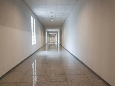 Beyaz duvarları, pencereleri ve kapıları olan uzun ve geniş koridor.