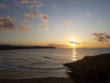 Los Locos sahilinde gün batımı. Bulutlar arasında. Güneş denize yansıdı. Los Locos Sahili, Suances, Cantabria, İspanya