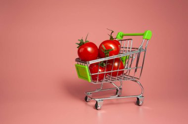 Pembe arka planda market arabasında küçük domatesler..