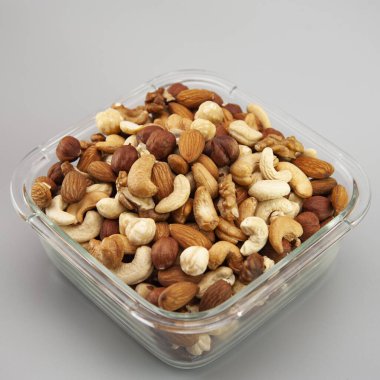 Gri arka planda cam bir tabakta çeşitli fındıklar.