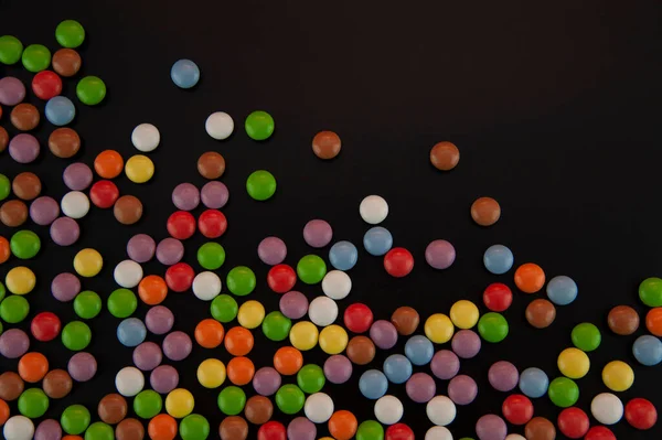 background in the form of colored candies sprinkled on a black background