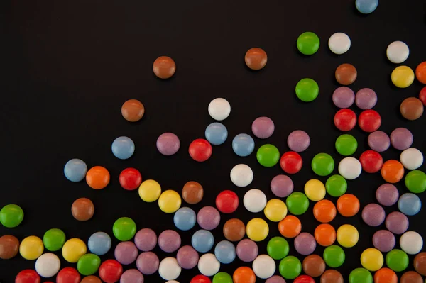 background in the form of colored candies sprinkled on a black background