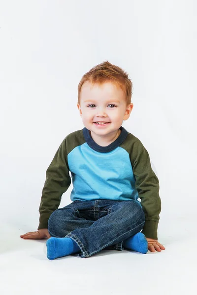 Pelirroja niño sentado en el suelo y sonriendo Imagen De Stock