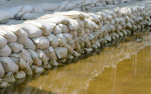 Sacchi di sabbia bianchi per la difesa dalle inondazioni ed è riflesso acqua marrone — Foto Stock