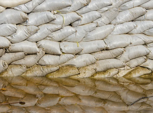 Białe worki z piaskiem na powódź obrony i jego odbicie brązowy wody — Zdjęcie stockowe