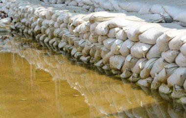 White sandbags for flood defense and it's reflection brown water clipart
