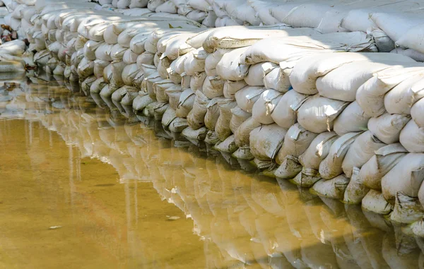 White sandbags for flood defense and it's reflection brown water — Stock Photo, Image