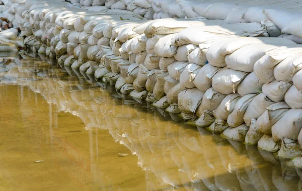 Sacchi di sabbia bianchi per la difesa dalle inondazioni ed è riflesso acqua marrone — Foto Stock