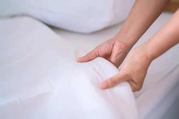 Female Hand set up white bed sheet in bedroom or maid hands making bed in a hotel room.