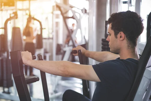 Handsome man lowering weight of fitness machine and working out in the fitness gym.