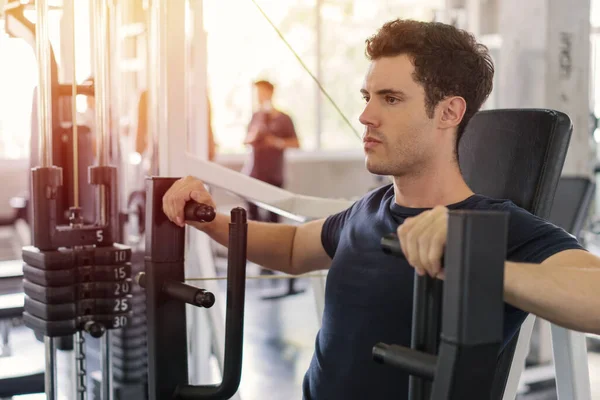 Handsome man lowering weight of fitness machine and working out in the fitness gym.