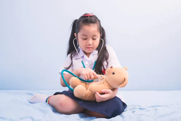 医者になるために人形で遊んでいる医療用制服の可愛い女の子と聴診器 子供の夢は医師としてのキャリアの概念になり — ストック写真