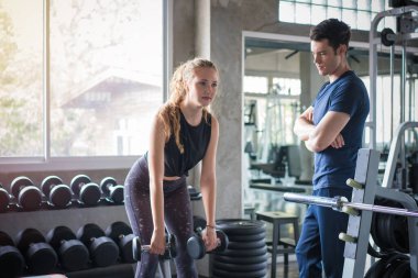 Kişisel antrenörle taburede oturan genç bir kadın spor salonundaki kadın müşteri için spor yapıyor..