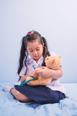 Tıp üniformalı ve steteskoplu güzel kızlar doktor olmak için oyuncak bebekle oynuyorlar. Çocuk, doktor kariyer konsepti olmayı hayal ediyor..