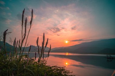 Güneş doğarken yansıması mükemmel olan dağ gölü manzarası. Pembe pastel gökyüzü, arka planda tepeler ve suya yansıyan güzel dağ manzarası. Doğa gölü manzarası