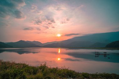 Güneş doğarken yansıması mükemmel olan dağ gölü manzarası. Pembe pastel gökyüzü, arka planda tepeler ve suya yansıyan güzel dağ manzarası. Doğa gölü manzarası