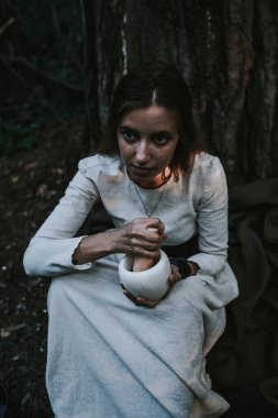 Kozalaklı bir ormanda, tarihi bir elbise giymiş bir kız.