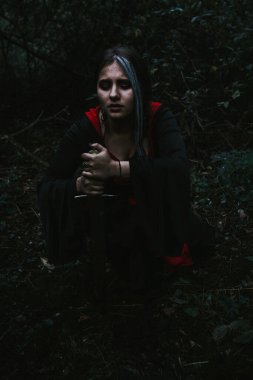 Kozalaklı bir ormanda, tarihi bir elbise giymiş bir kız.