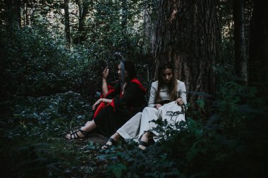 Kozalaklı bir ormanda, tarihi bir elbise giyen kızlar.