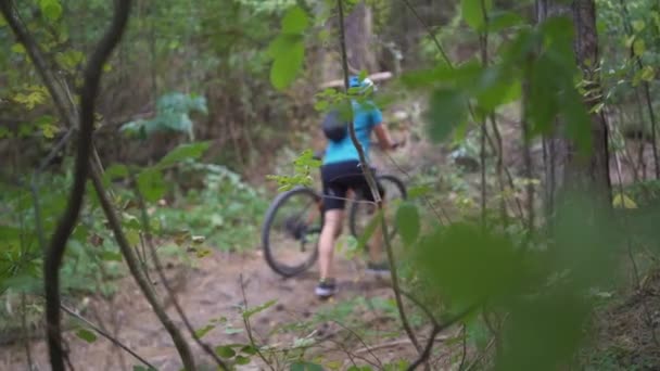 Genç dağ bisikletçisi ormanın tepesinde dağ bisikletini itiyor. — Stok video