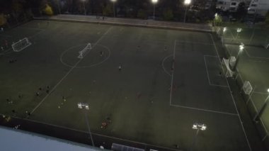 İnsanlar geceleri şehir parkındaki spor sahasında futbol oynuyorlar.