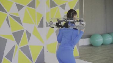 Bayan CrossFit eğitmeninin büyük aynanın önünde su torbasıyla çömelmesi.