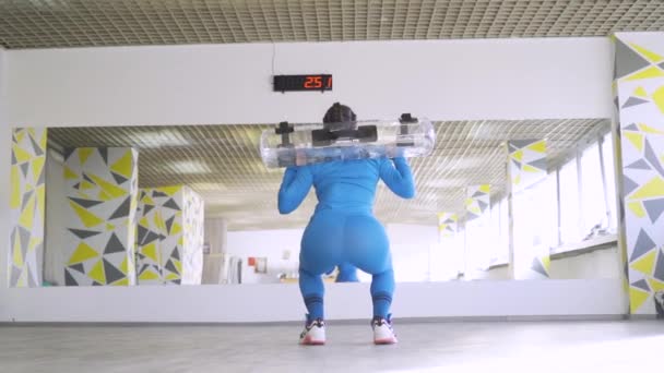 Задний вид прилегающей мускулистой женщины-тренера фитнеса, сидящей на корточках с гидромешком — стоковое видео