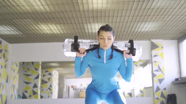 Brunette femme en bleu vêtements de sport accroupi avec sac d'alimentation en eau — Video