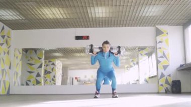 Atletik kadın su torbasını omuzlarında ağır çekimde tutarken zıplıyor.